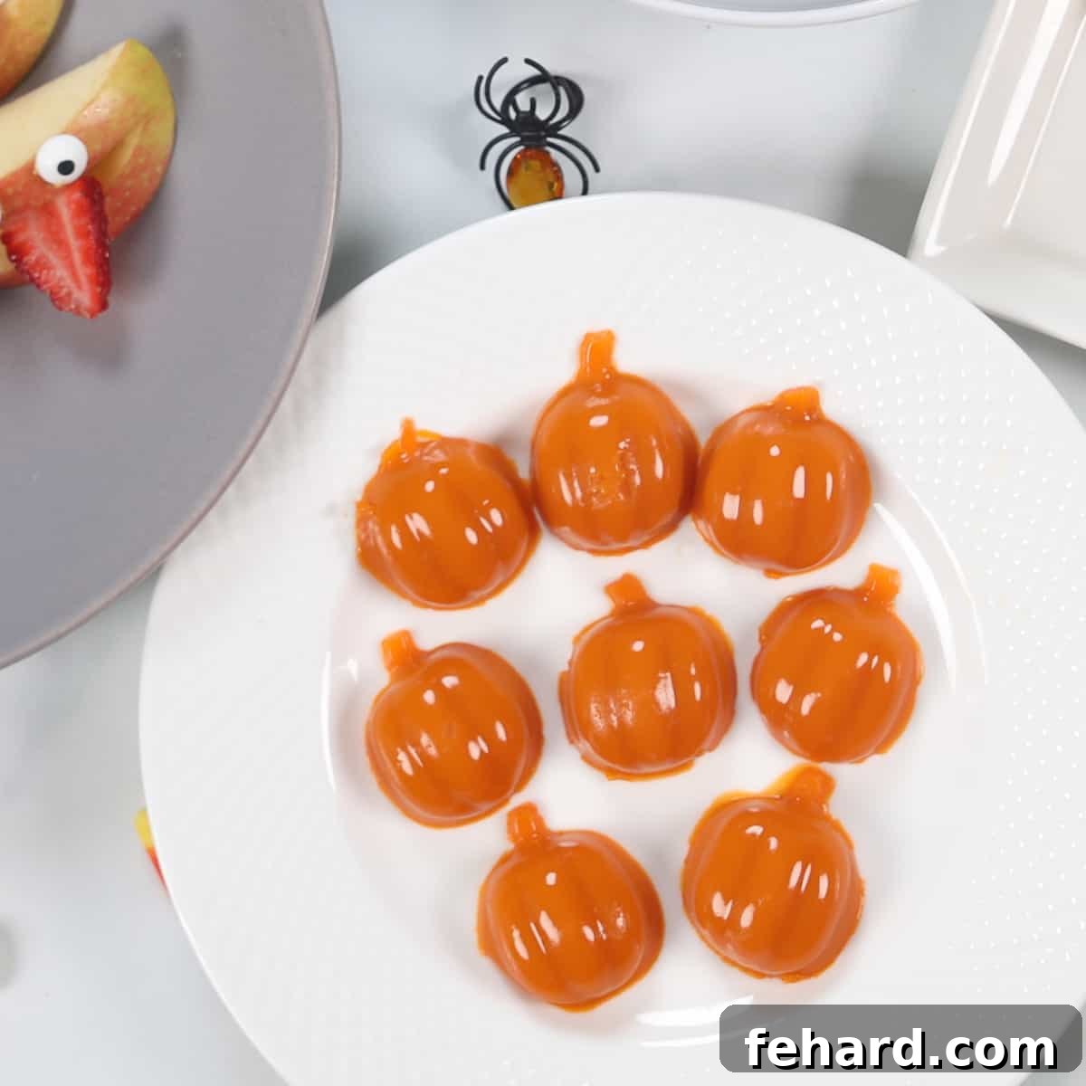 A handful of homemade pumpkin-shaped gummies, vibrant orange and slightly translucent, presented on a white plate.