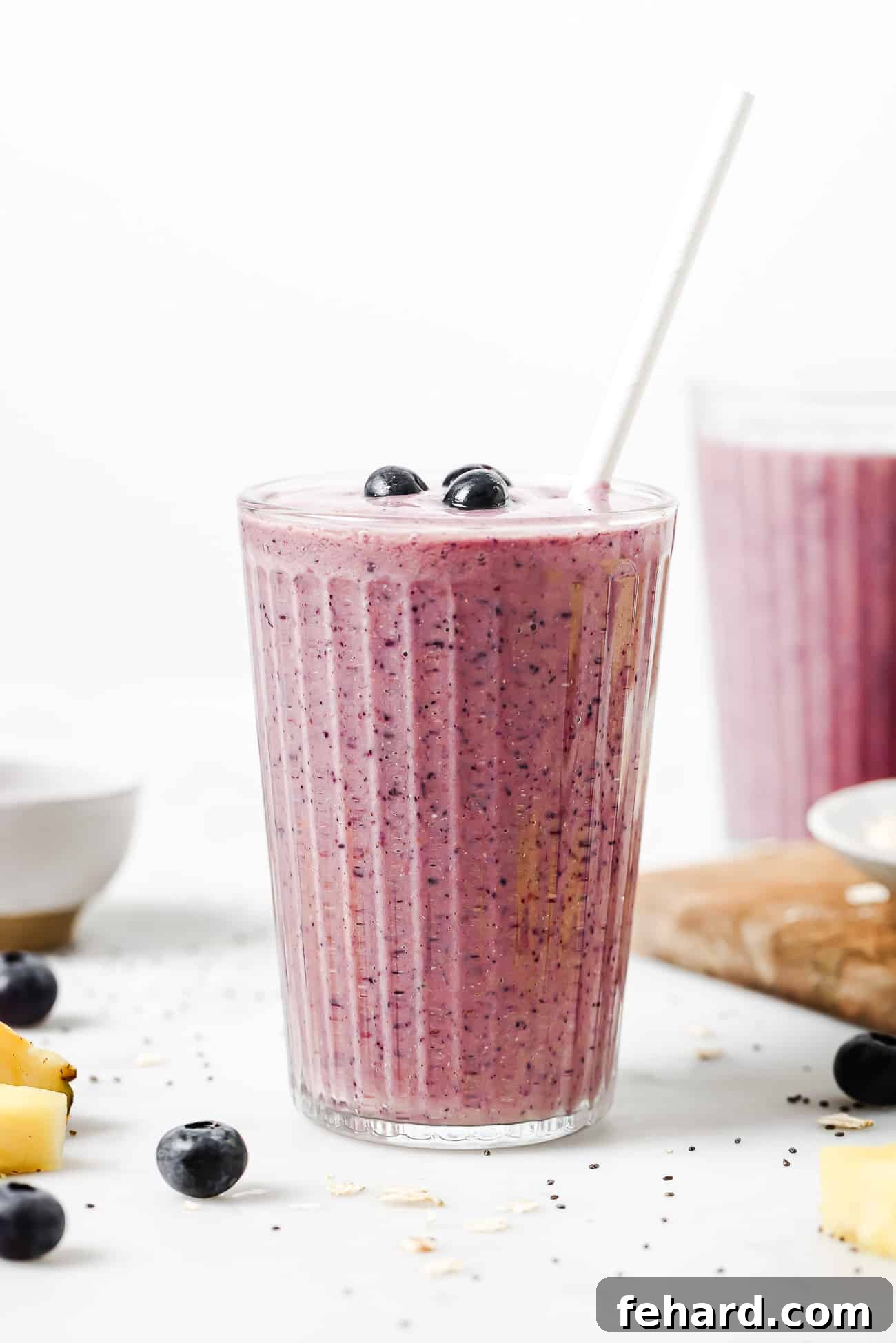 A tall glass filled with a creamy blueberry banana smoothie, garnished with fresh blueberries and a mint leaf.