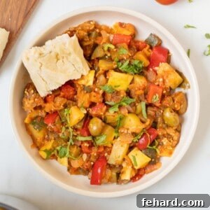 Thick Classic Ratatouille dished up in bowl topped with basil and served with crusty bread on the side.