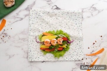 Vibrant Veggie Wraps 4 Tea towel with spring roll wrapper on it topped with lettuce, peppers, mango, carrots, mint, and shrimp before rolling into spring roll.