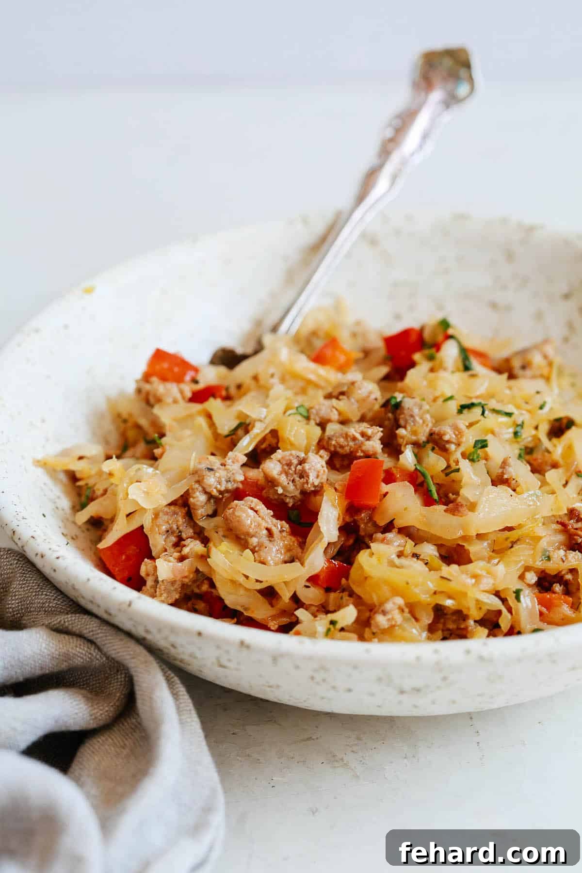 Hearty Cabbage and Sausage Skillet 4 close up of a metal fork in bowl filled with cooked cabbage, sausage, and bell peppers