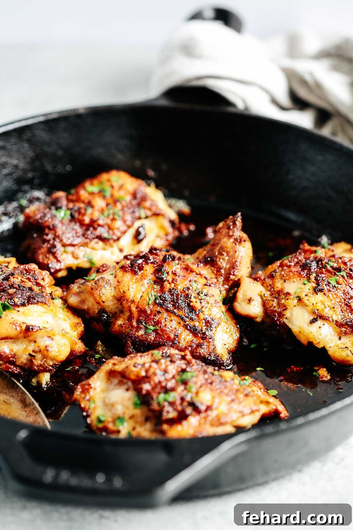 Closeup view of cooked chicken thighs in a skillet with butter sauce, garnished with fresh herbs.