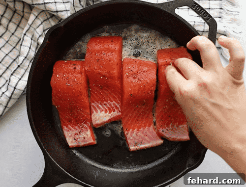 Close-up of salmon fillets searing skin-side down in a cast iron skillet