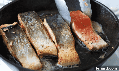 Close-up of a salmon fillet flipped to the flesh side up in a cast iron skillet, continuing to cook