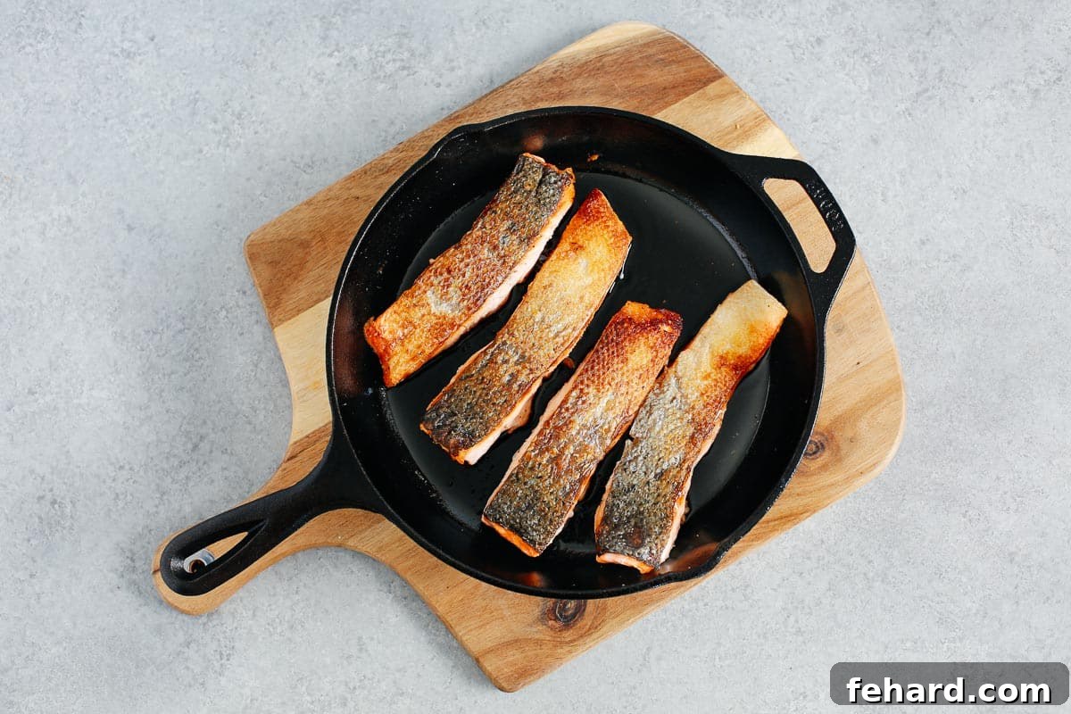 Crispy Golden Pan Seared Salmon 5 Four salmon fillets with beautifully crispy skin sizzling in a cast iron skillet, golden and delicious