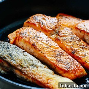 Four pan-seared salmon fillets presented on a white plate after cooking, garnished and ready to eat