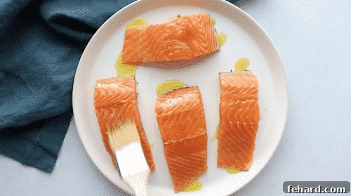 overhead view of a salmon being brushed with olive oil on a white plate