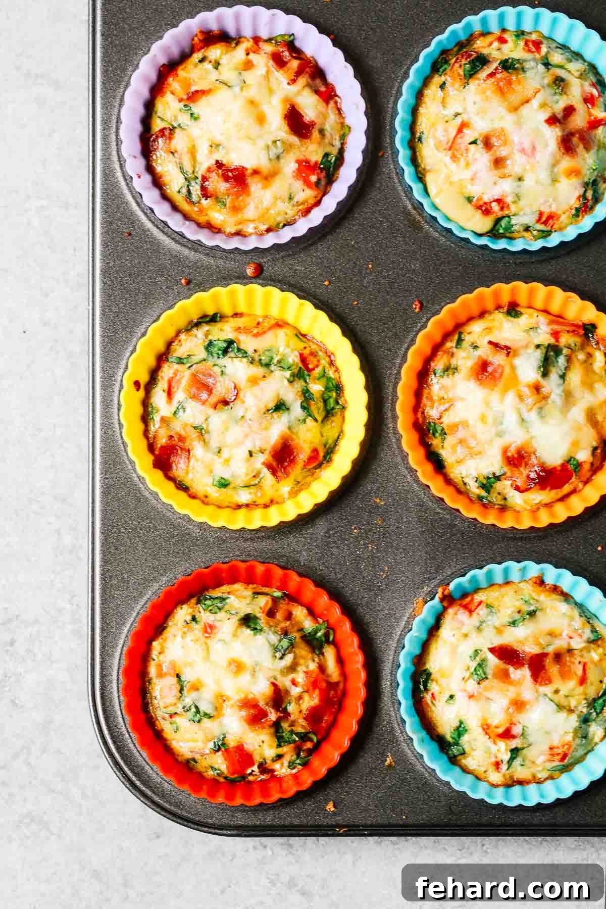 Overhead shot of six individual breakfast quiches, baked to golden perfection in a muffin pan, showcasing their delicious fillings.