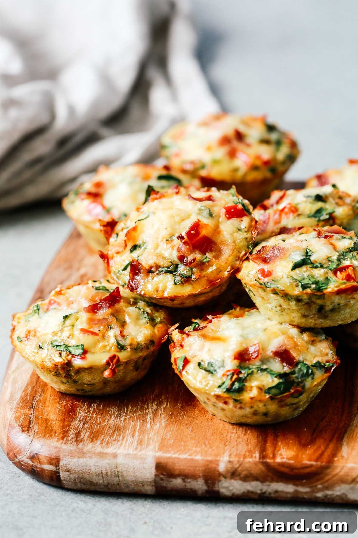 A wooden cutting board holds an assortment of freshly baked egg and vegetable muffins, showcasing their hearty and healthy appeal.