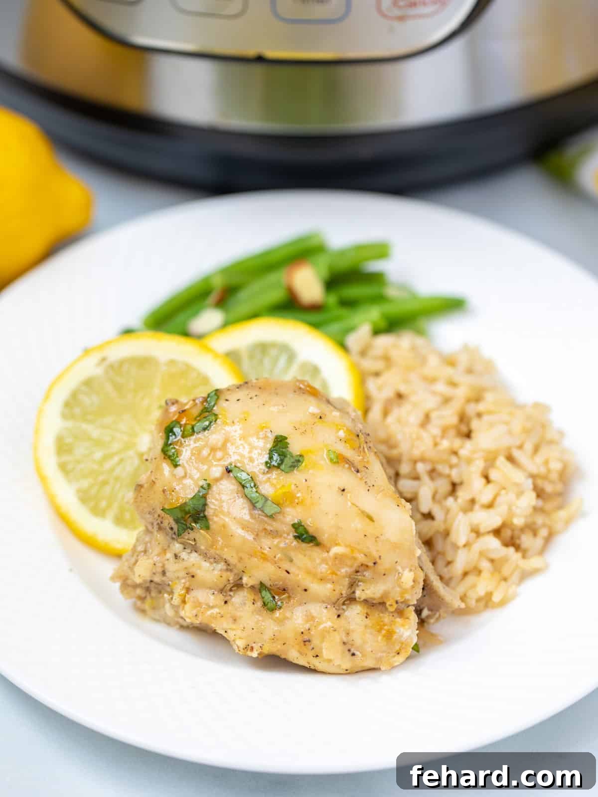 Lemon chicken on white plate with brown rice and green beans. A perfectly cooked Instant Pot Lemon Garlic Chicken dish served with healthy sides.