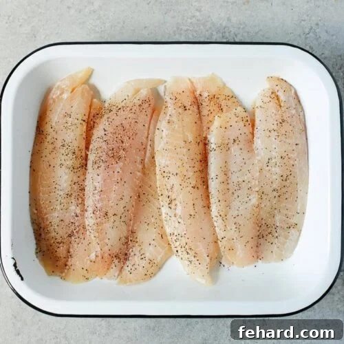 Raw tilapia in a baking sheet, seasoned and ready for sauce.
