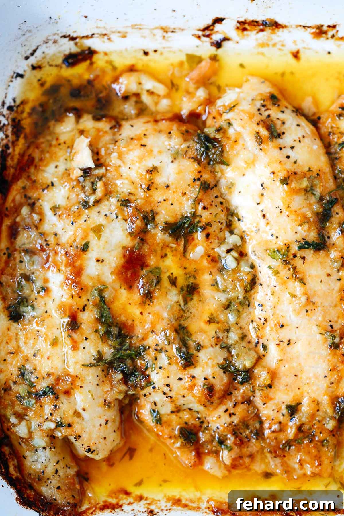 Close-up view of golden-brown baked tilapia with garlic butter sauce, garnished with fresh parsley.