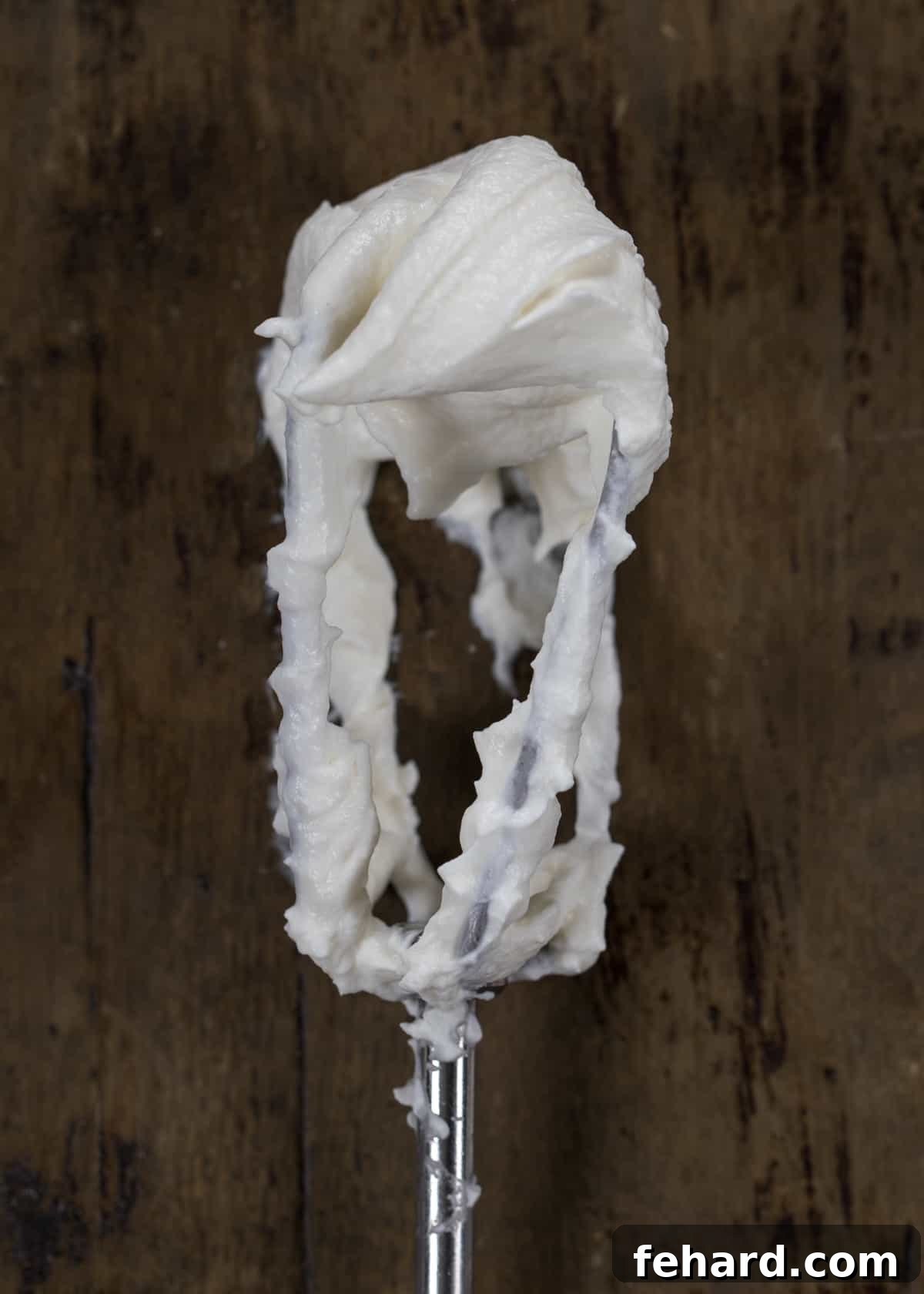 A mixer beater covered in whipped cream, demonstrating perfect soft peaks.
