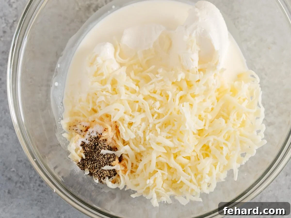 Golden Cauliflower Gratin 5 A large glass bowl containing cream cheese, half-and-half, shredded mozzarella, garlic powder, onion powder, salt, and pepper, ready to be mixed.