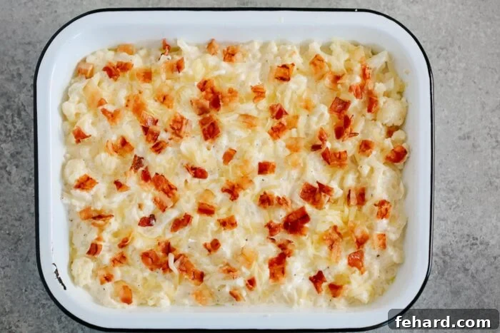 Golden Cauliflower Gratin 7 Cauliflower and cheese mixture scooped into a white casserole dish, topped with additional mozzarella and cooked bacon bits, ready for baking.