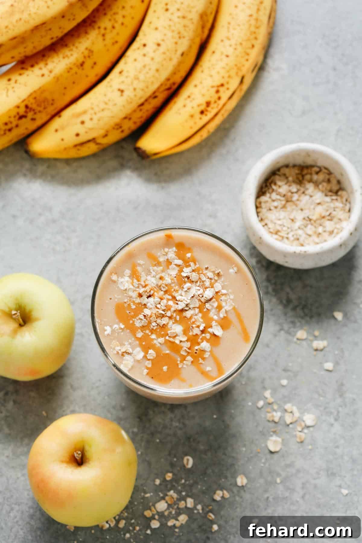cup of apple smoothie with oats sprinkled on top with bananas, apples, and oats placed beside it