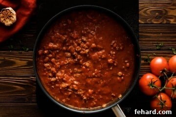 Meat sauce for homemade lasagna in a large skillet, combined with water and ready for layering.