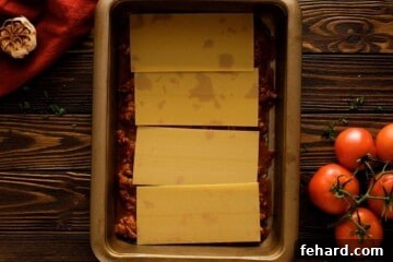 Meat sauce and 4 uncooked lasagna noodles layered in a baking dish, forming the first layer of homemade lasagna.