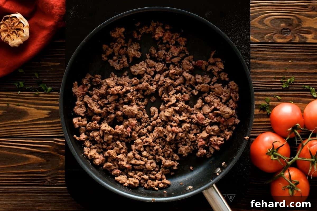 Ground beef being sautéed in a skillet, breaking into small pieces for a homemade lasagna meat sauce.