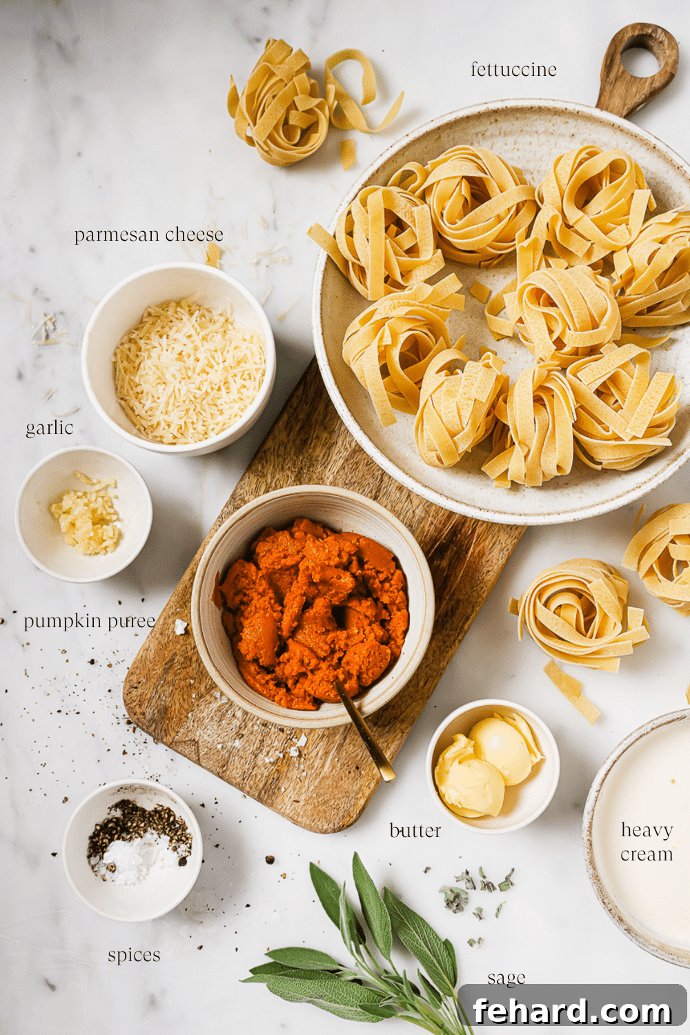 An overhead view of prepped ingredients for pumpkin alfredo, including pumpkin puree, cream, butter, garlic, and sage, arranged on a white countertop with a wooden cutting board.