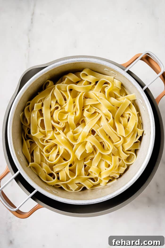 An overhead view of cooked and drained fettuccine noodles resting in a colander.