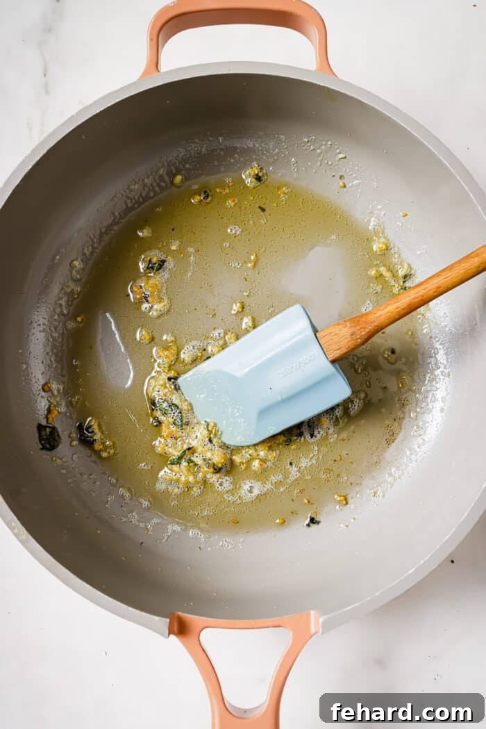An overhead view of butter melting in a skillet, with fresh sage leaves and minced garlic infusing the butter.