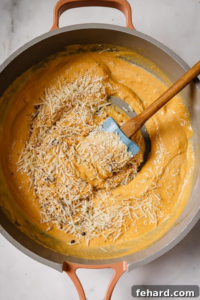 Parmesan cheese, salt, and black pepper being added to the simmering pumpkin and cream sauce in the skillet.