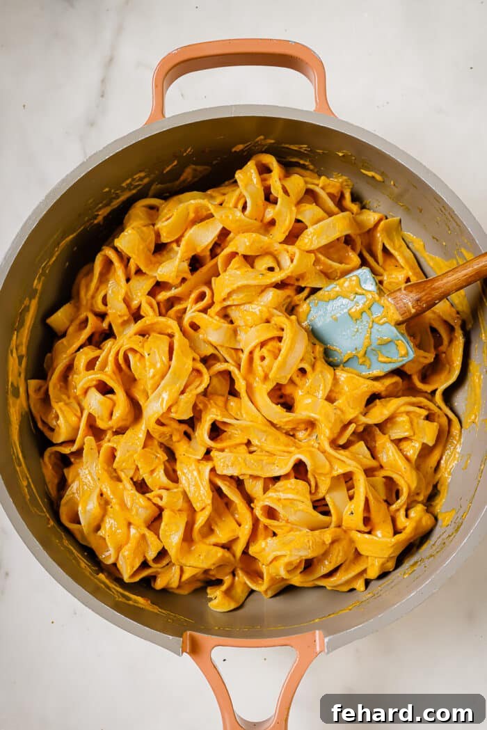 Cooked fettuccine noodles being added directly into the pumpkin alfredo sauce in the skillet.