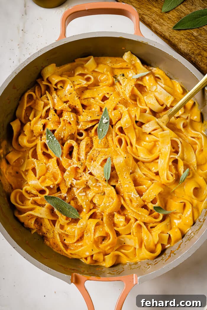A serving of pumpkin alfredo fettuccine pasta in a bowl, garnished with fresh sage leaves and grated Parmesan cheese.