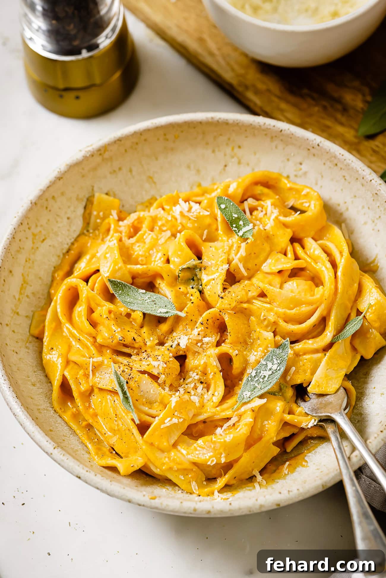 A full bowl of creamy pumpkin alfredo sauce over fettuccine noodles, garnished with a sprig of fresh sage.