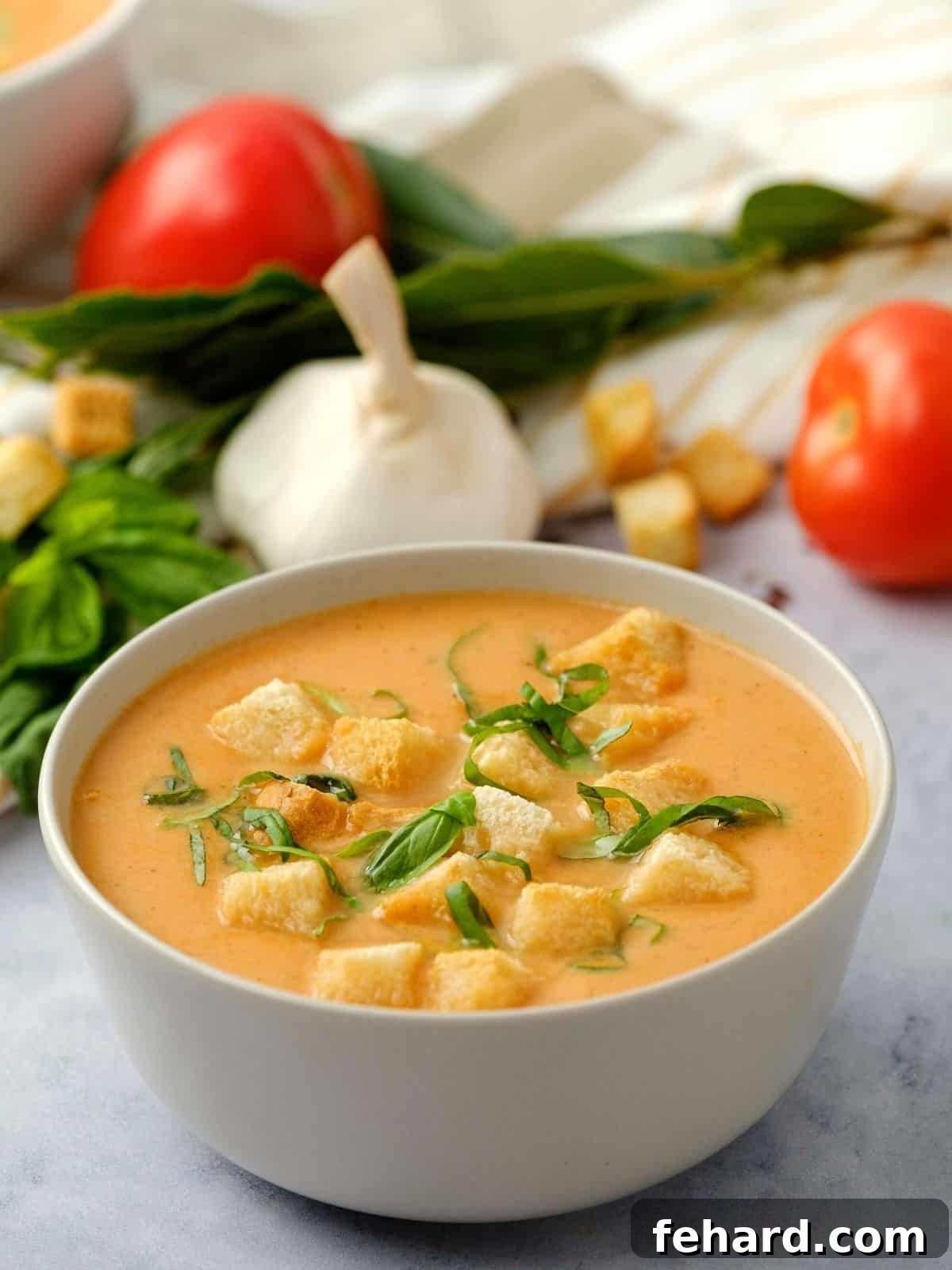 A steaming bowl of creamy Instant Pot Tomato Soup, generously topped with golden croutons and fresh basil leaves. The background features fresh tomatoes and garlic, hinting at the simple, wholesome ingredients.