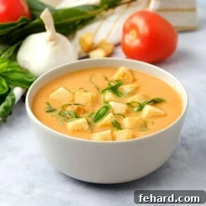 Bowl of creamy tomato soup topped with croutons and basil.