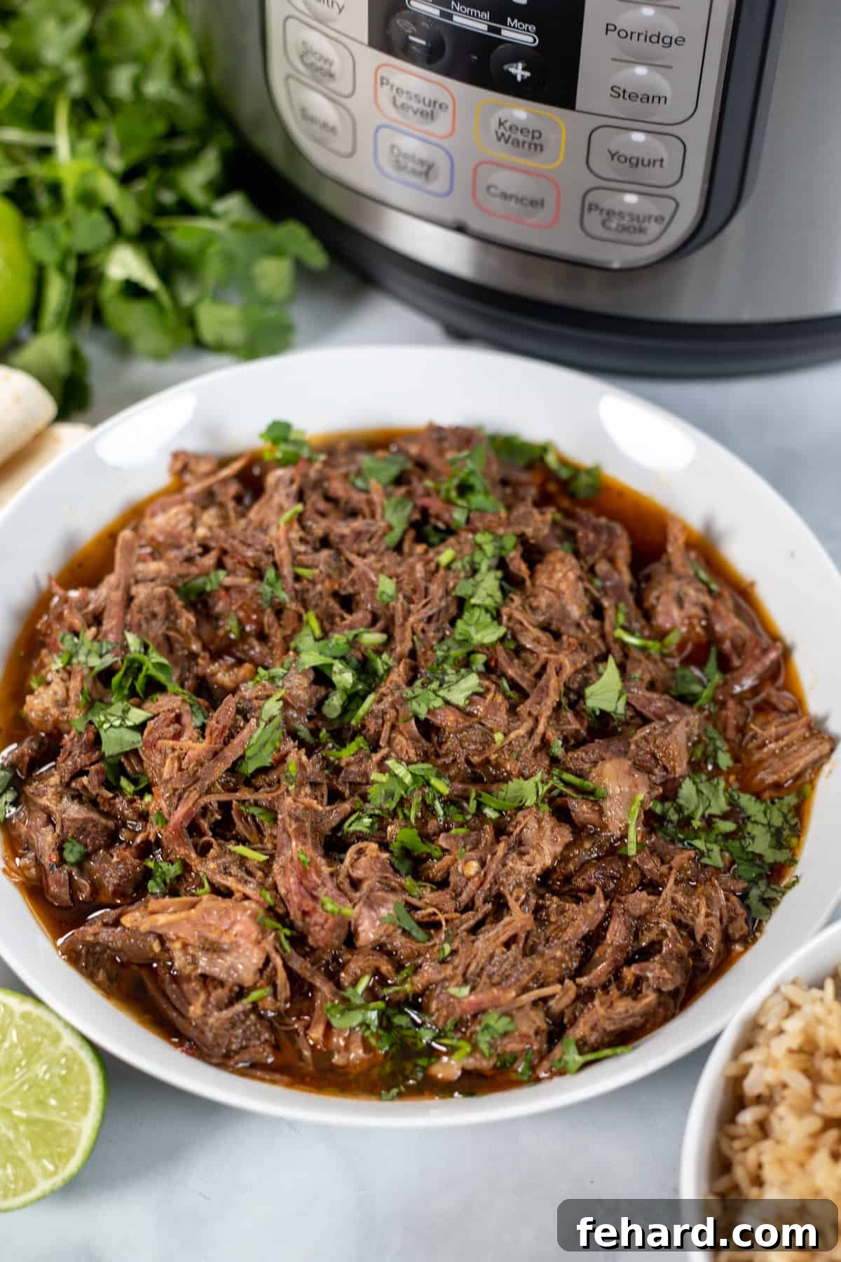 Instant Pot Barbacoa A white bowl brimming with shredded barbacoa, positioned next to a gleaming Instant Pot.