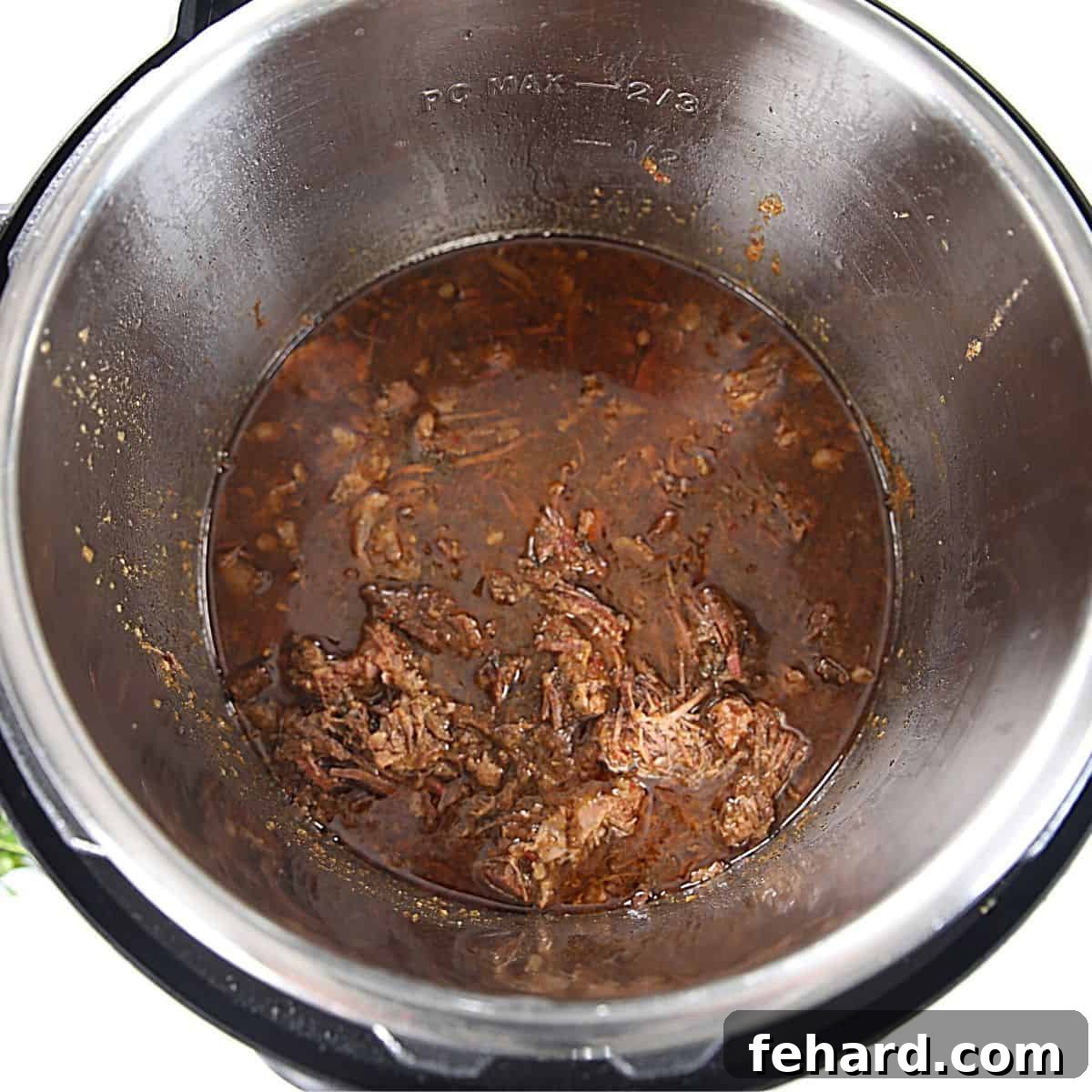 Instant Pot Barbacoa Beef Shredded beef simmering in a rich Mexican sauce within the Instant Pot's inner pot.