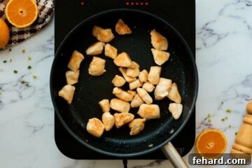 Browned chicken in saute pan next to sliced fresh oranges.
