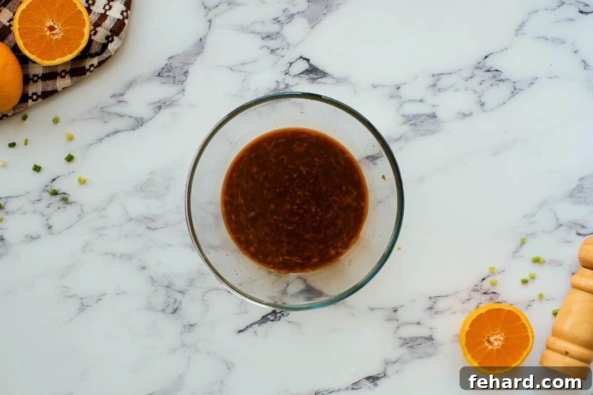 A small glass bowl containing the freshly whisked orange sauce, vibrant in color and smooth in consistency, positioned on a wooden surface and ready to be incorporated into the chicken dish.