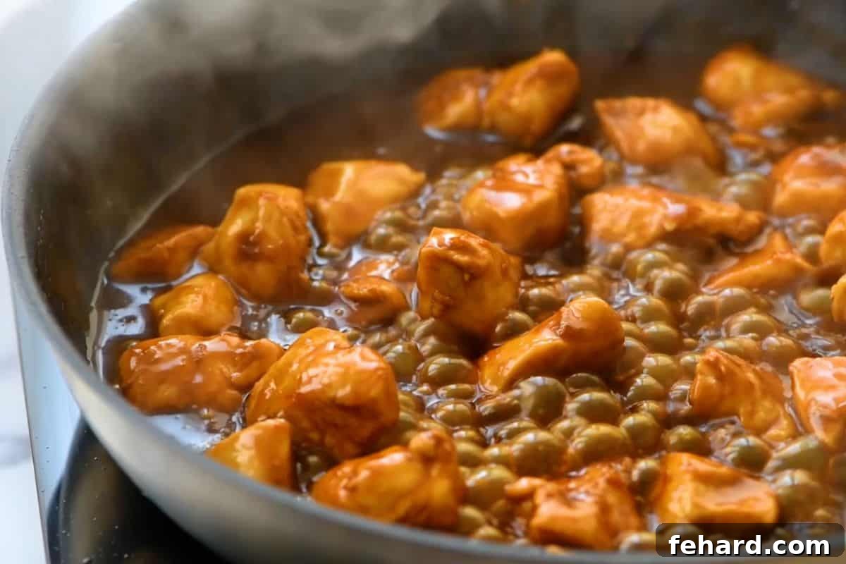 A skillet filled with succulent orange chicken pieces simmering gently in the rich, vibrant orange sauce, creating a mouthwatering visual of the finished dish.