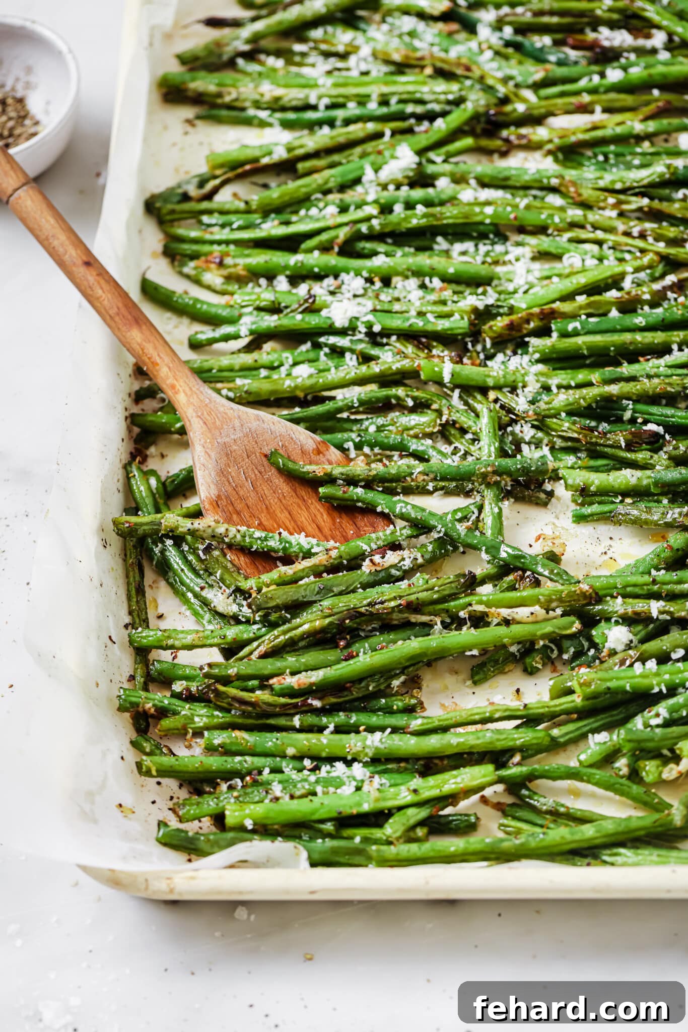 Garlic Parmesan Green Beans 6 Close up of a baking sheet filled with perfectly roasted parmesan green beans, fresh out of the oven, with a crispy, golden cheese topping.
