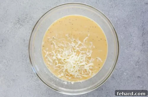 Close-up image of eggs and shredded cheese being whisked together in a clear glass bowl, preparing the liquid base for the breakfast casserole.