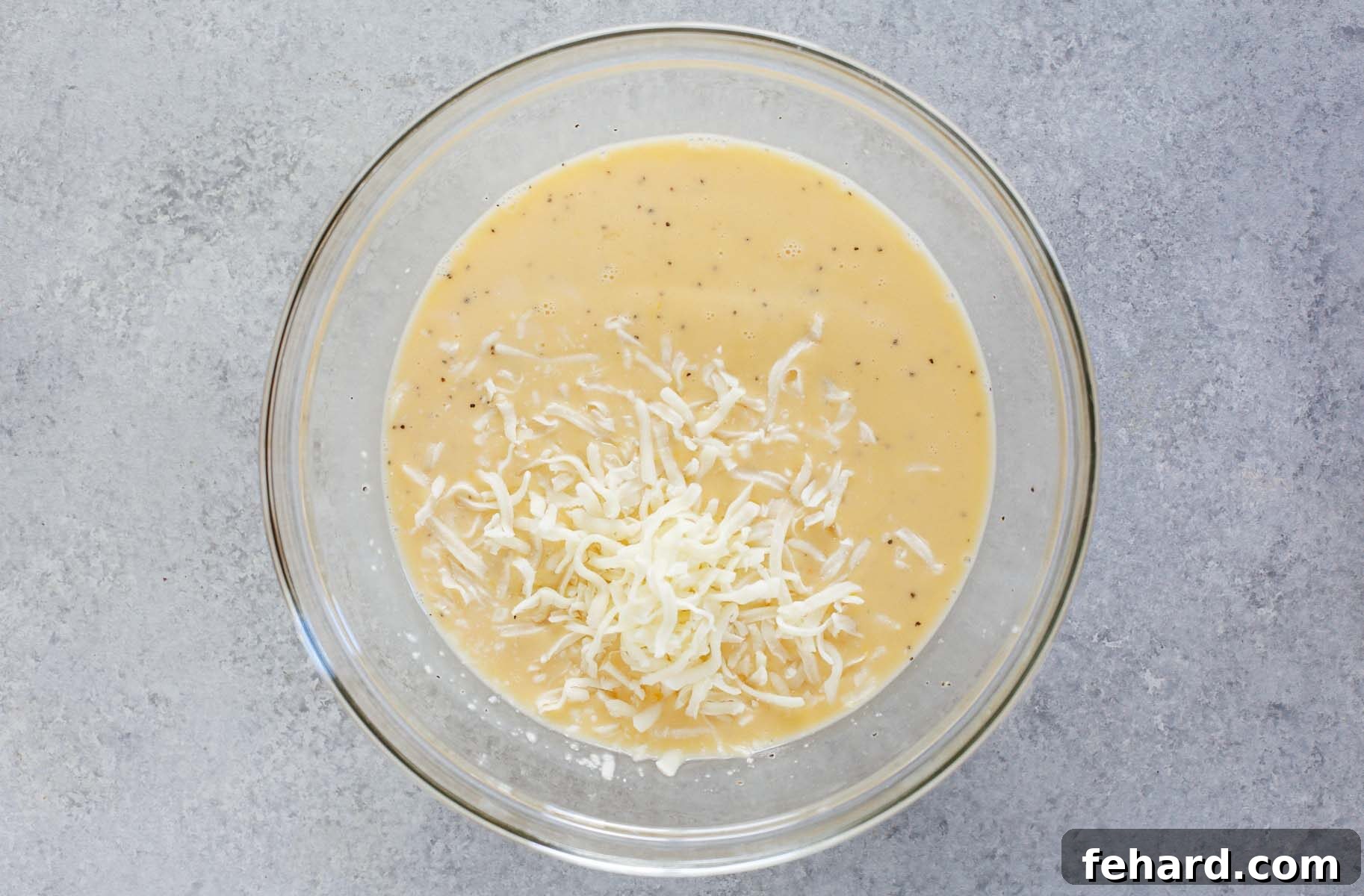 Close-up image of eggs and shredded cheese being whisked together in a clear glass bowl, ready for the breakfast casserole.