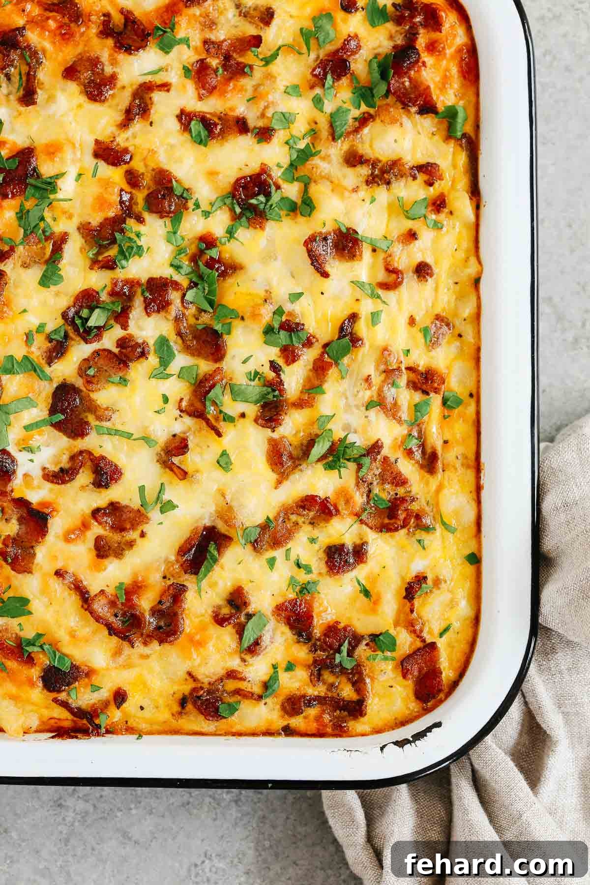 Close up of a golden-brown Sausage and Potato Breakfast Casserole in a pan, steaming hot and ready to be served, garnished with fresh herbs.