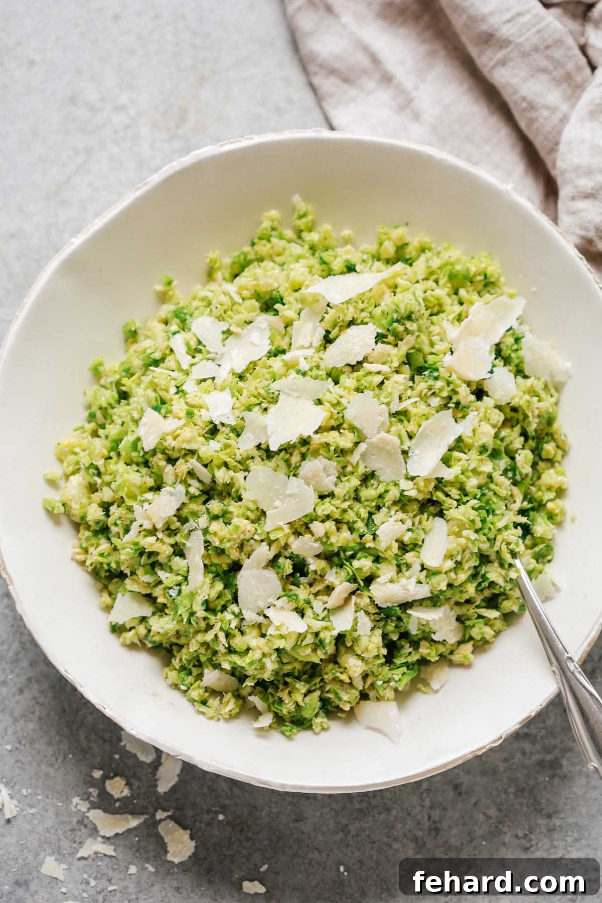 close up of a Parmesan Brussels Sprouts Salad with a spoon and shaved parmesan on top, highlighting the fresh texture
