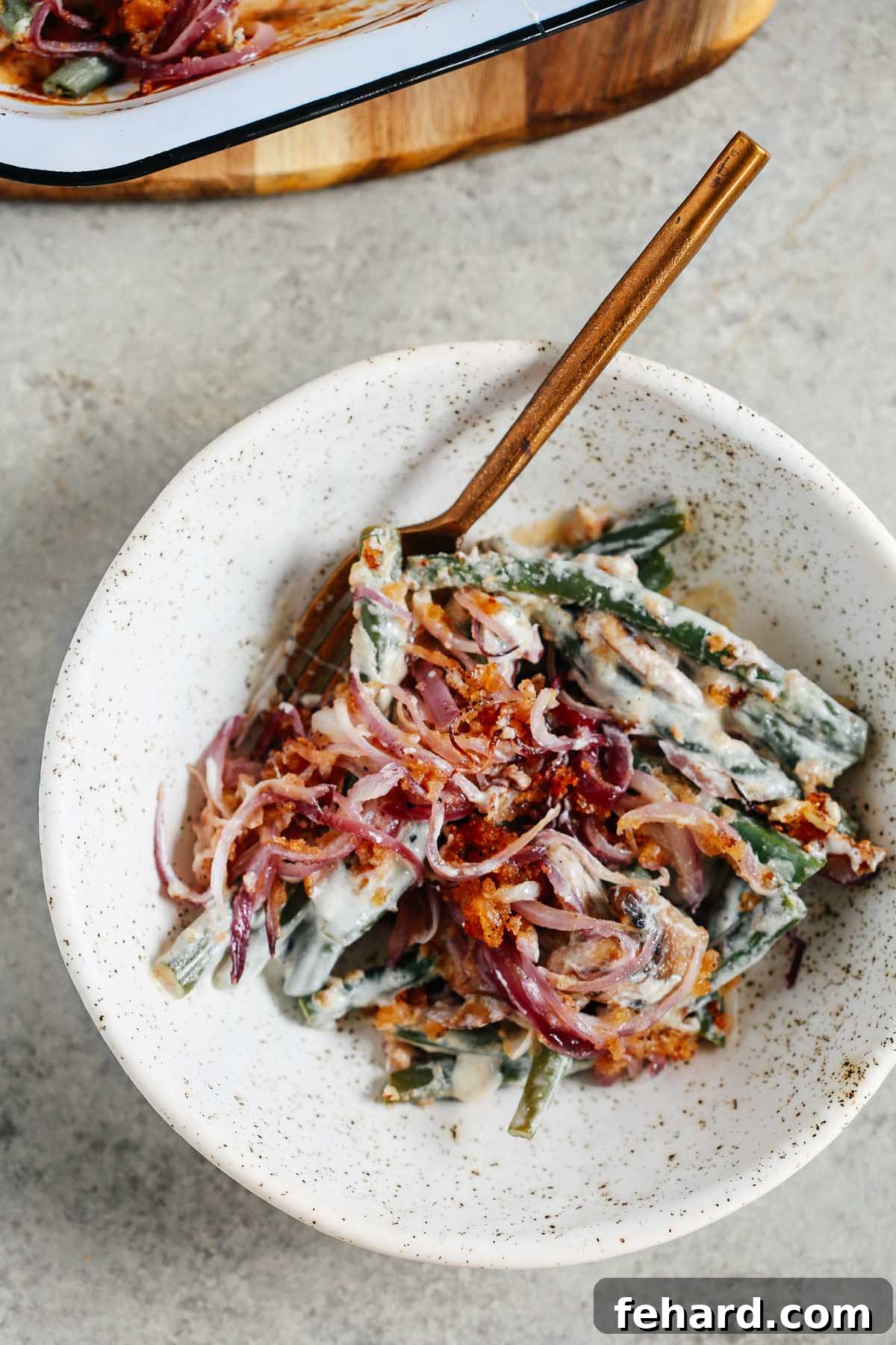 Overhead photo of Healthier Green Bean Casserole Recipe in a white bowl with a gold fork inside. 