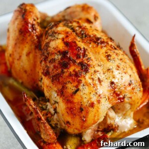 Photo of a garlic herb butter roast chicken inside of a white roasting pan.