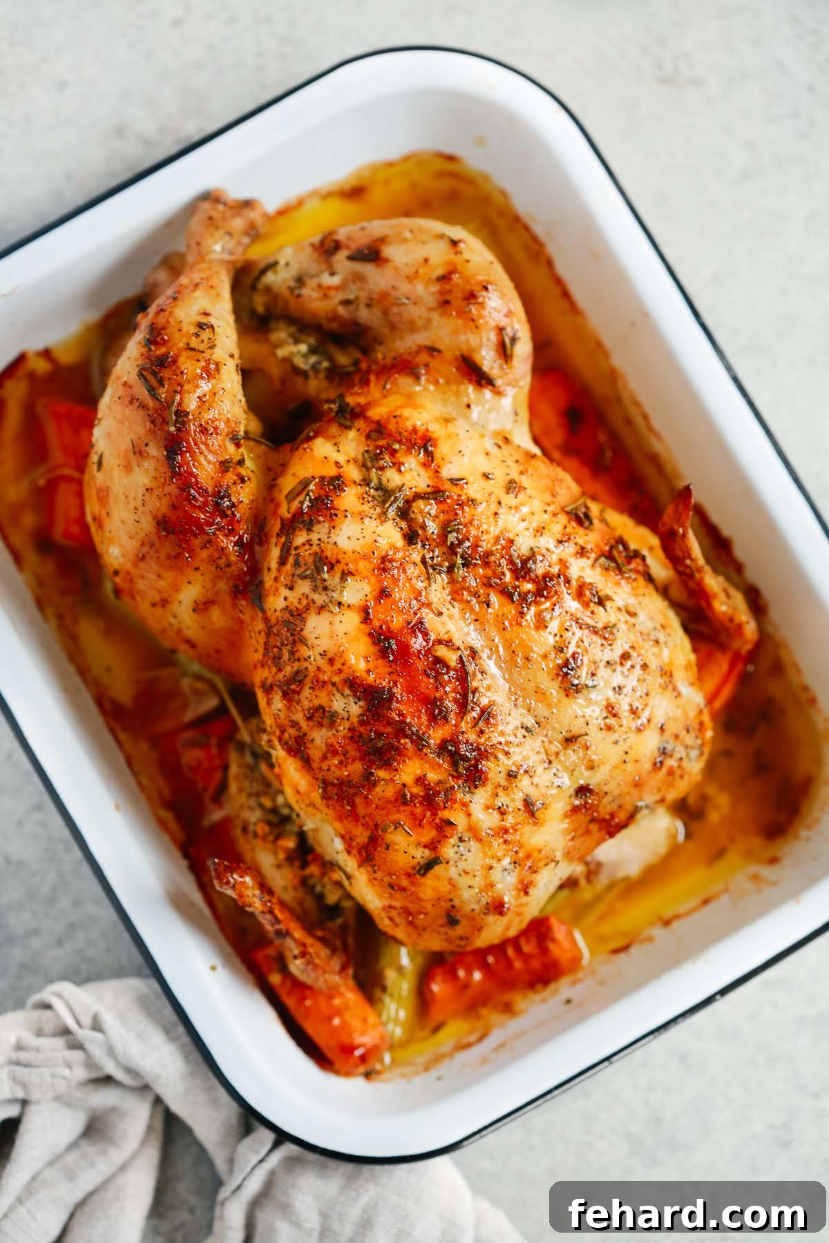 An overhead view of a beautifully golden-brown roasted whole chicken, perfectly cooked and resting in a white roasting pan.