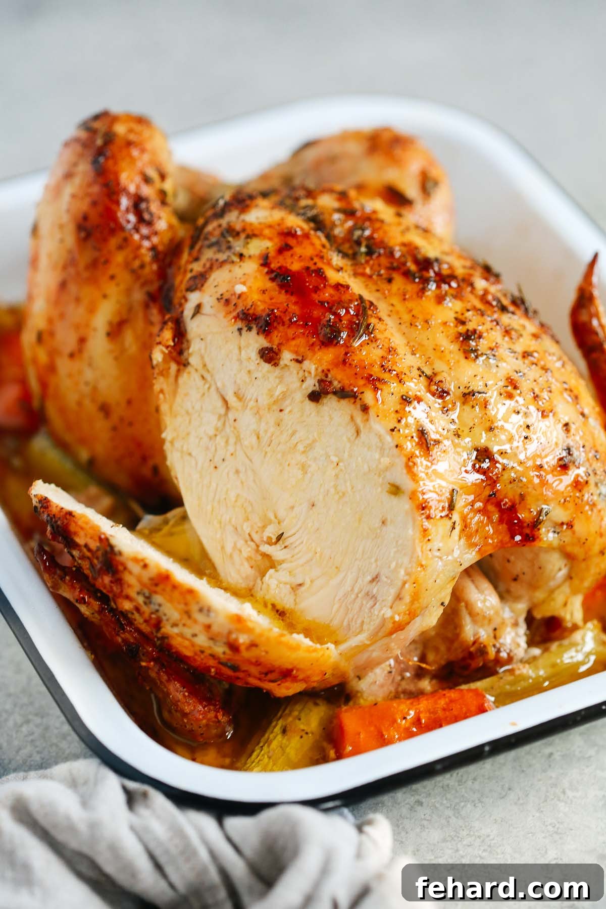 A close-up photo of a roasted whole chicken with a portion of the breast expertly sliced, revealing its tender, juicy interior.