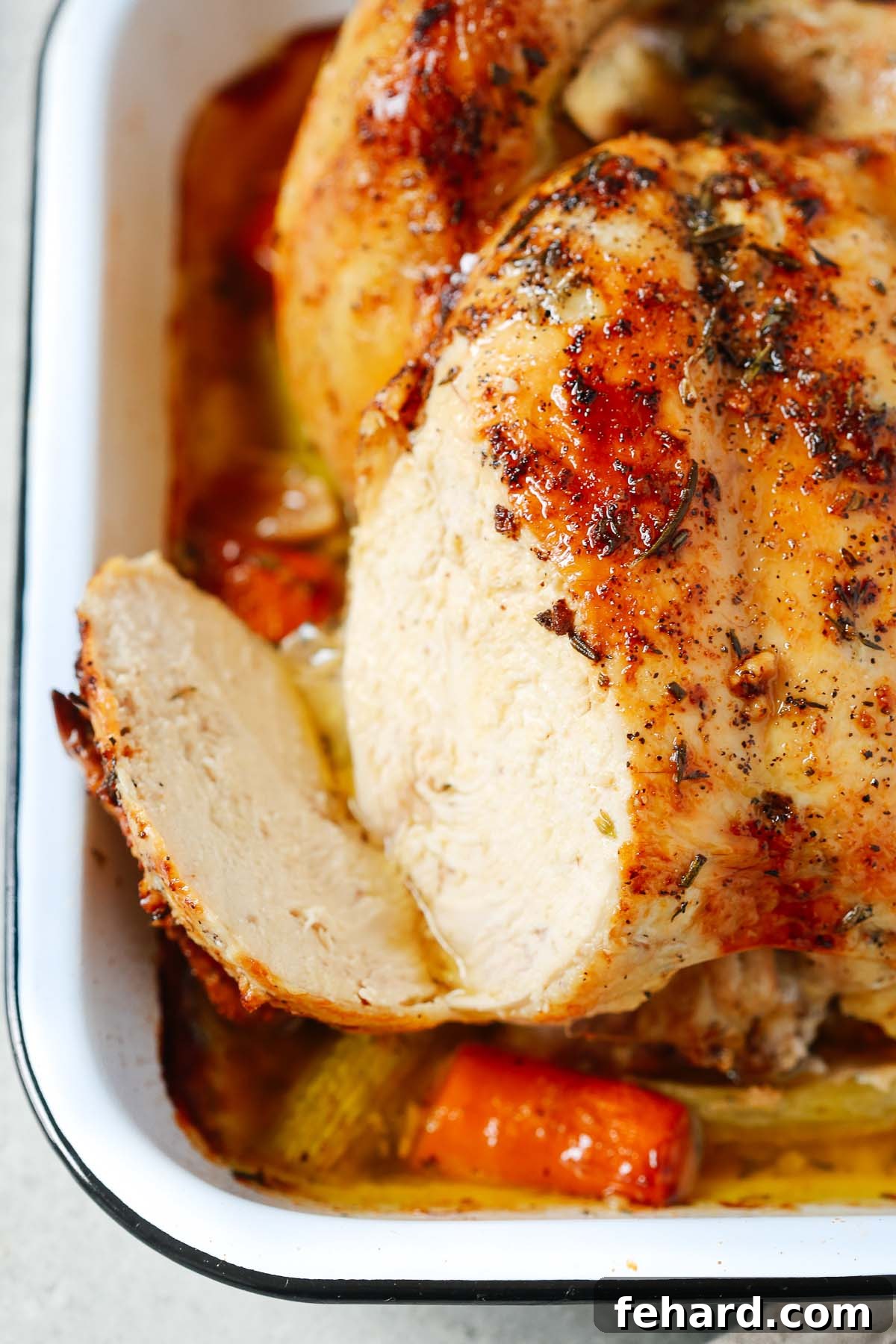 A close-up image of a roasted whole chicken with a section of its breast sliced open, showcasing the tender, juicy meat.