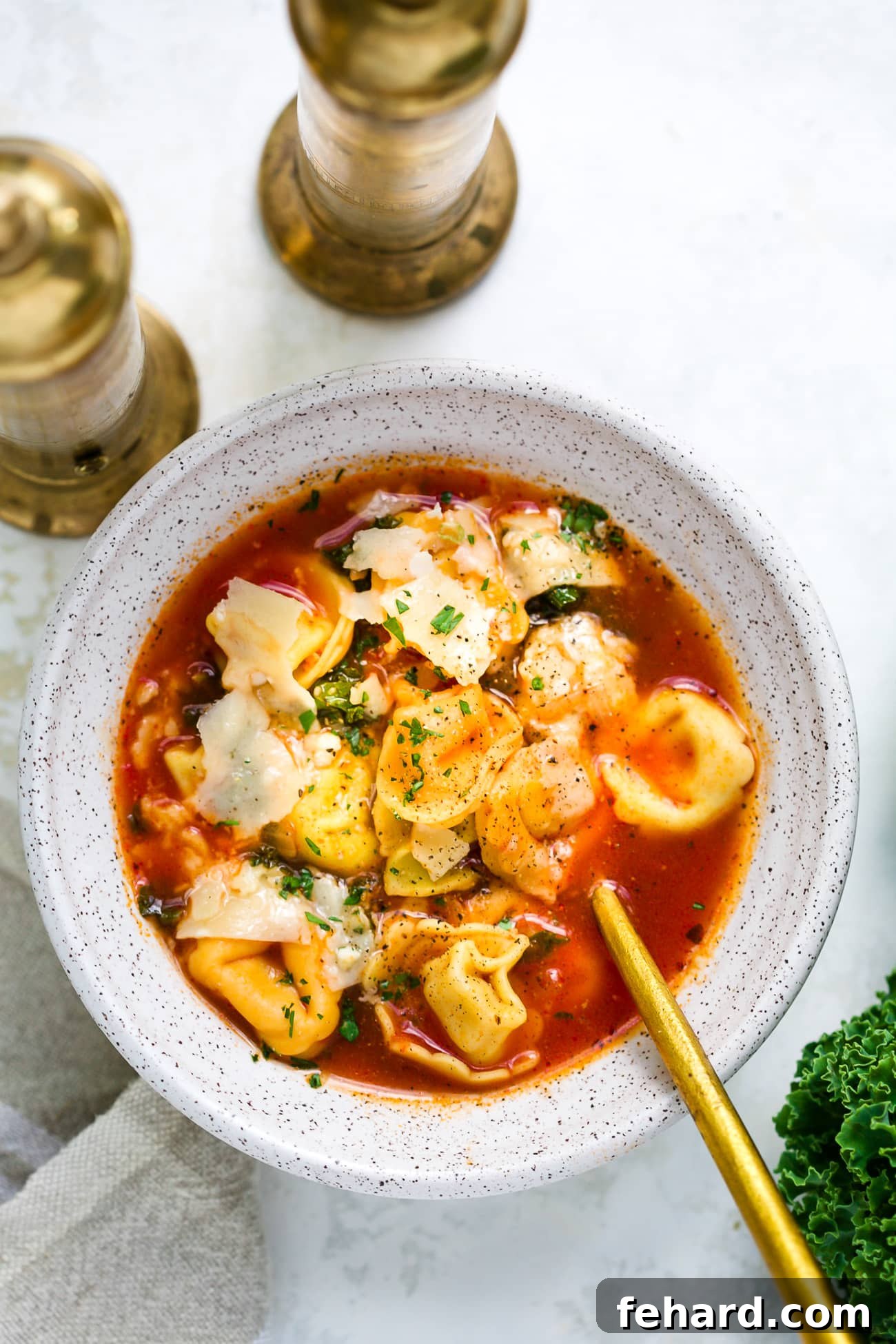 A beautifully presented bowl of kale tortellini soup, garnished with fresh basil leaves and grated Parmesan cheese, ready to be enjoyed.