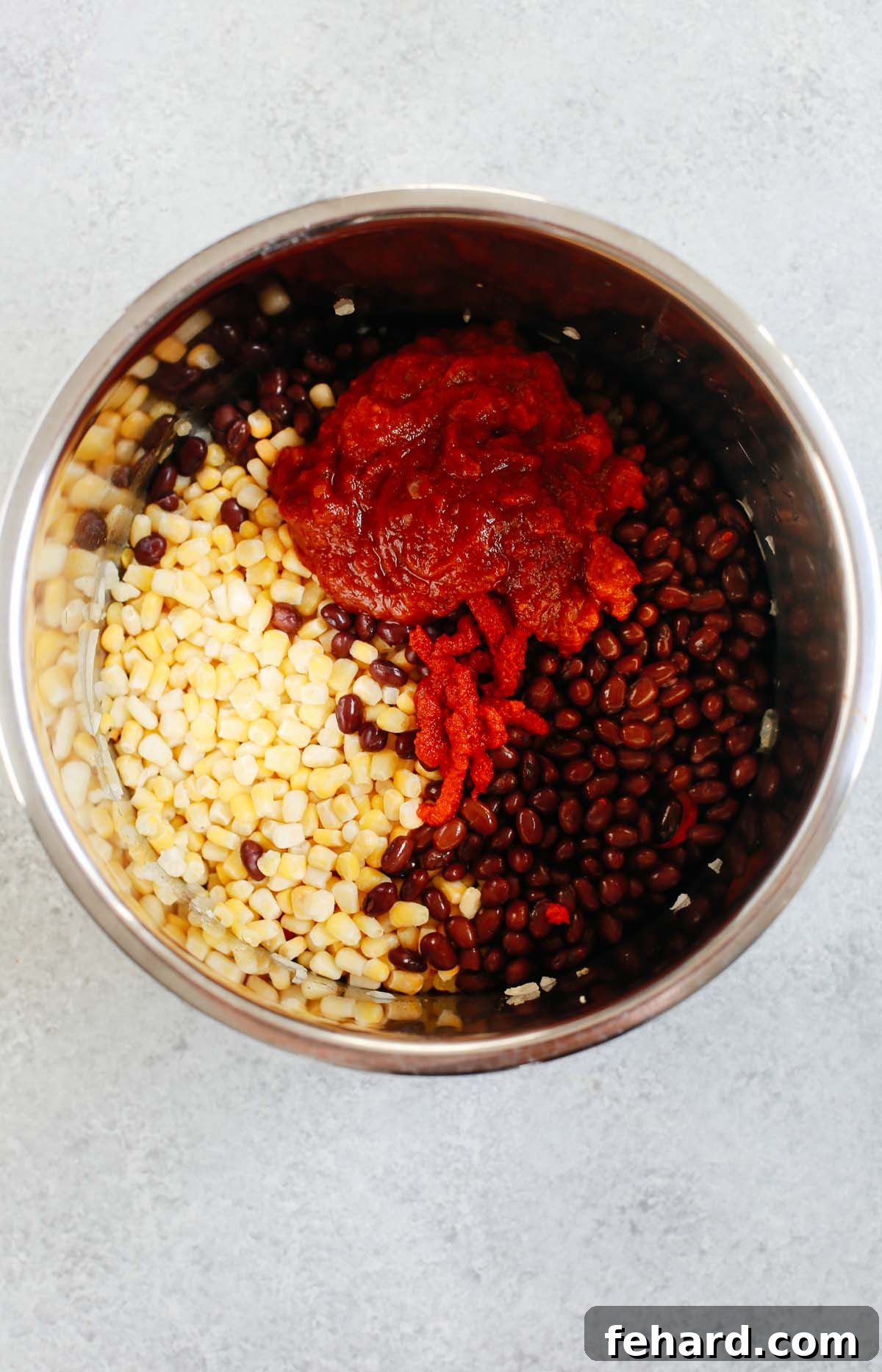 An Instant Pot liner filled with corn, black beans, tomato sauce, and tomato paste, ready for cooking.