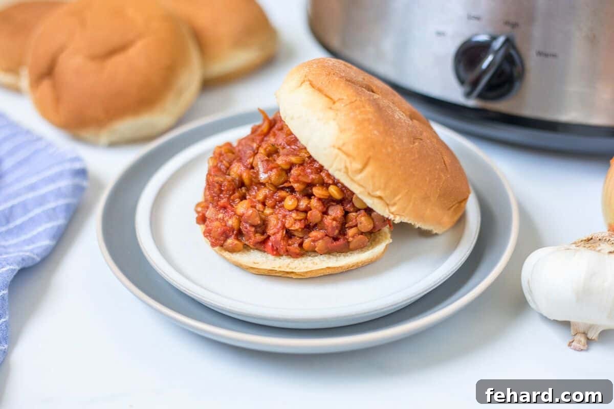 Delicious Lentil Sloppy Joes served on a bun on a plate, with a slow cooker visible in the background.
